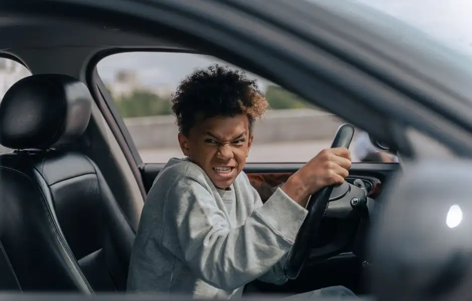 Un jeune conducteur au volant d’une citadine, regard attentif, ceinture attachée, en ville.